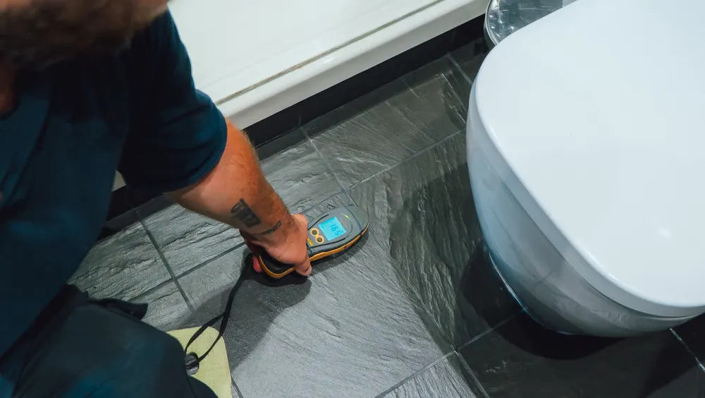 A moisture meter held against a tiled bathroom surface