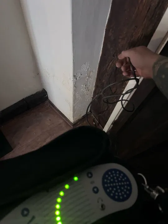 Acoustic listening equipment on the floor beside a damp wall corner and a dark timber post